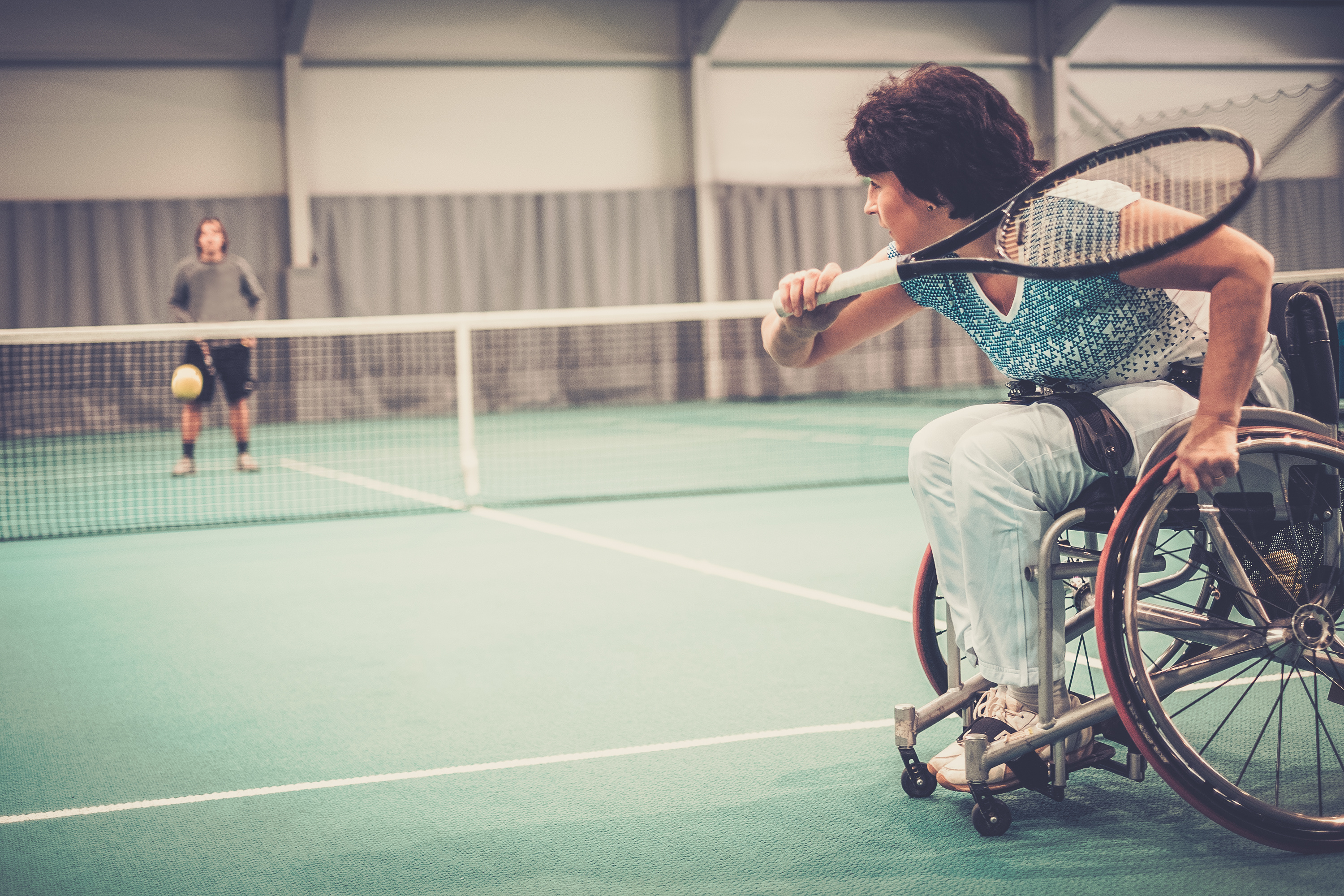 Disabled mature woman on wheelchair playing tennis on tennis cou